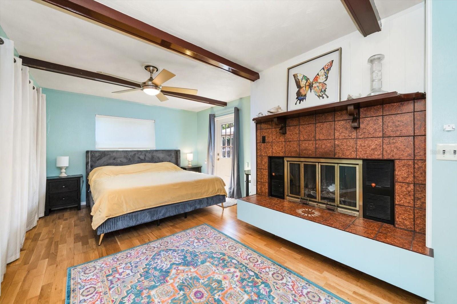 Primary bedroom with fireplace, beamed ceilings, and access door to backyard deck