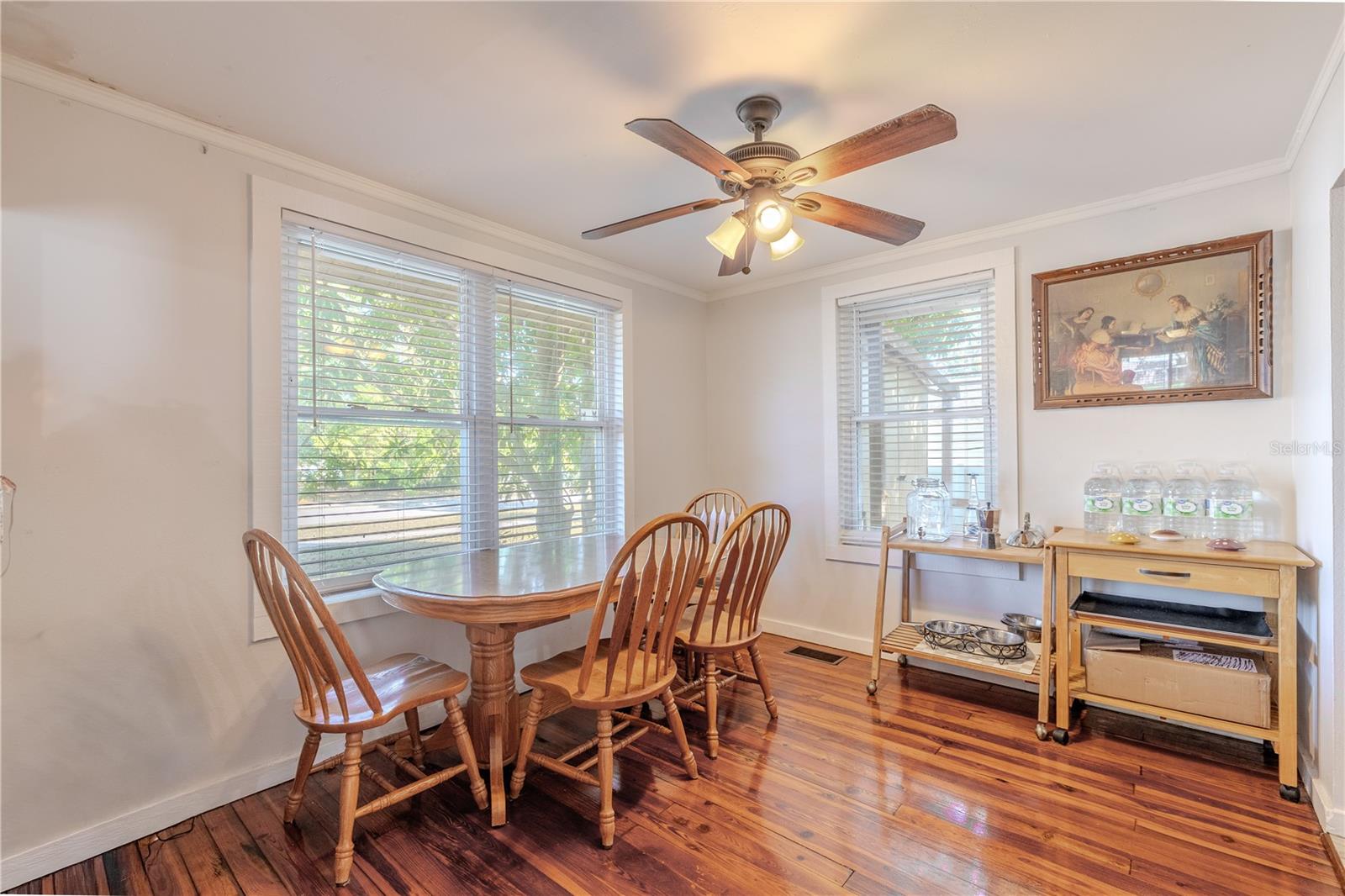 As you step into the dining area from the living room, you're greeted by a bright, welcoming space filled with natural light from multiple windows. The warm original wood flooring continues seamlessly into this room, enhancing its cozy, inviting feel. A ceiling fan provides added comfort, and the layout offers plenty of room for a family dining table or casual breakfast setup. This light-filled dining space sits just off the kitchen, creating an easy flow for meals and entertaining.