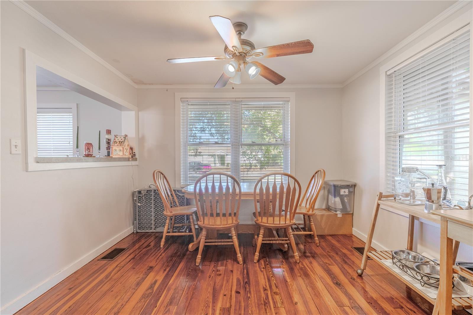This bright dining room, viewed from the kitchen passthrough, features beautiful original wood flooring and abundant natural light from multiple windows. A ceiling fan adds comfort, while the open connection to both the kitchen and living areas enhances the home’s easy, flowing layout. The space comfortably accommodates a family dining table and offers a warm, inviting atmosphere perfect for everyday meals or entertaining.