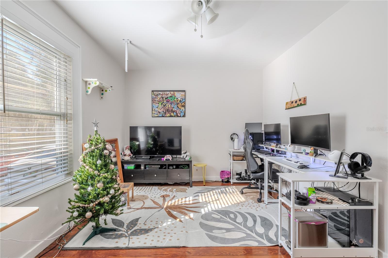 This view from the full bathroom showcases the spacious layout of the first-floor bedroom, offering plenty of room for a bed, seating area, or home office setup. Natural light fills the space through a large window, highlighting the beautiful wood floors and neutral wall color. The room’s generous size and flexible layout make it ideal for guests, multigenerational living, or a dedicated workspace. Direct bathroom access adds convenience and privacy.