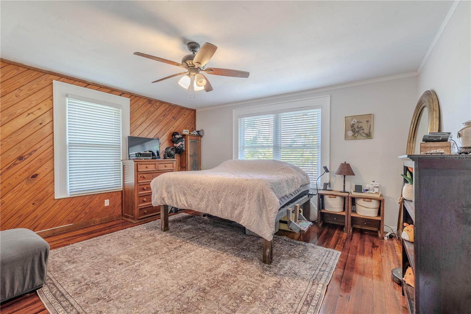 his spacious second-floor master bedroom features charming wood accent paneling, crown molding, and beautifully maintained wood floors that add warmth and character. Large windows invite abundant natural light, creating a bright and comfortable retreat. The generous layout provides ample space for a full bedroom suite, making this master an inviting place to relax and unwind.