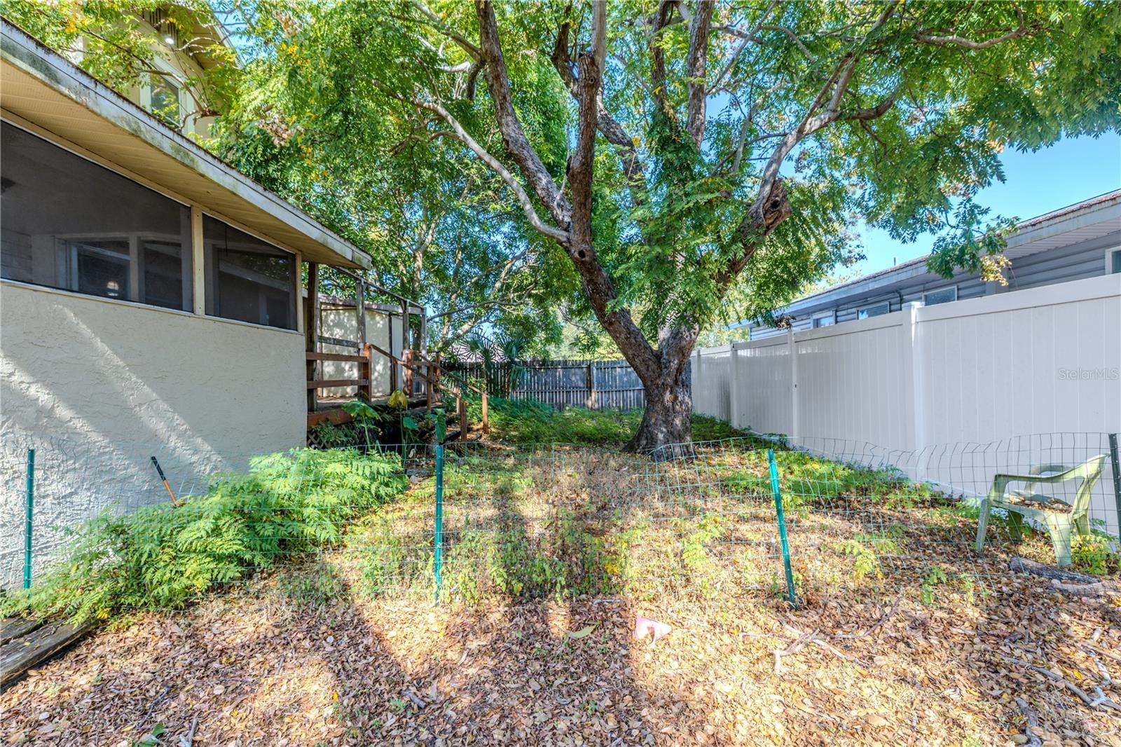 This backyard view highlights a peaceful, tree-shaded outdoor space with mature landscaping and plenty of room for gardening, pets, or play. The fully fenced perimeter provides privacy and security, while the large established tree creates a natural canopy of shade. The deck and screened-in porch are easily accessible from the yard, making this an inviting area for outdoor living and relaxation.