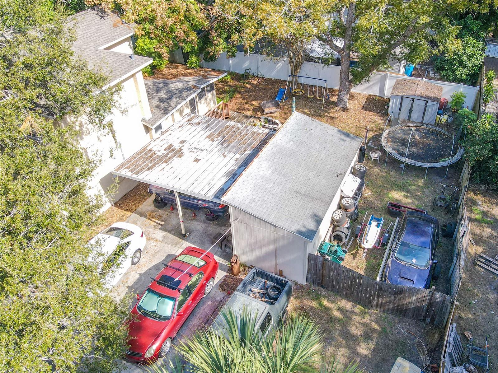 This aerial perspective highlights the property’s extensive outdoor features, including a covered carport and a sizable workshop—ideal for storage, projects, or hobbies. The fenced backyard includes a storage shed, additional open storage space, and a double-gated fence entrance that provides easy access for vehicles, trailers, equipment or storing a boat or RV. Mature trees offer shade and privacy, making this a functional and versatile outdoor area suited for a variety of needs.