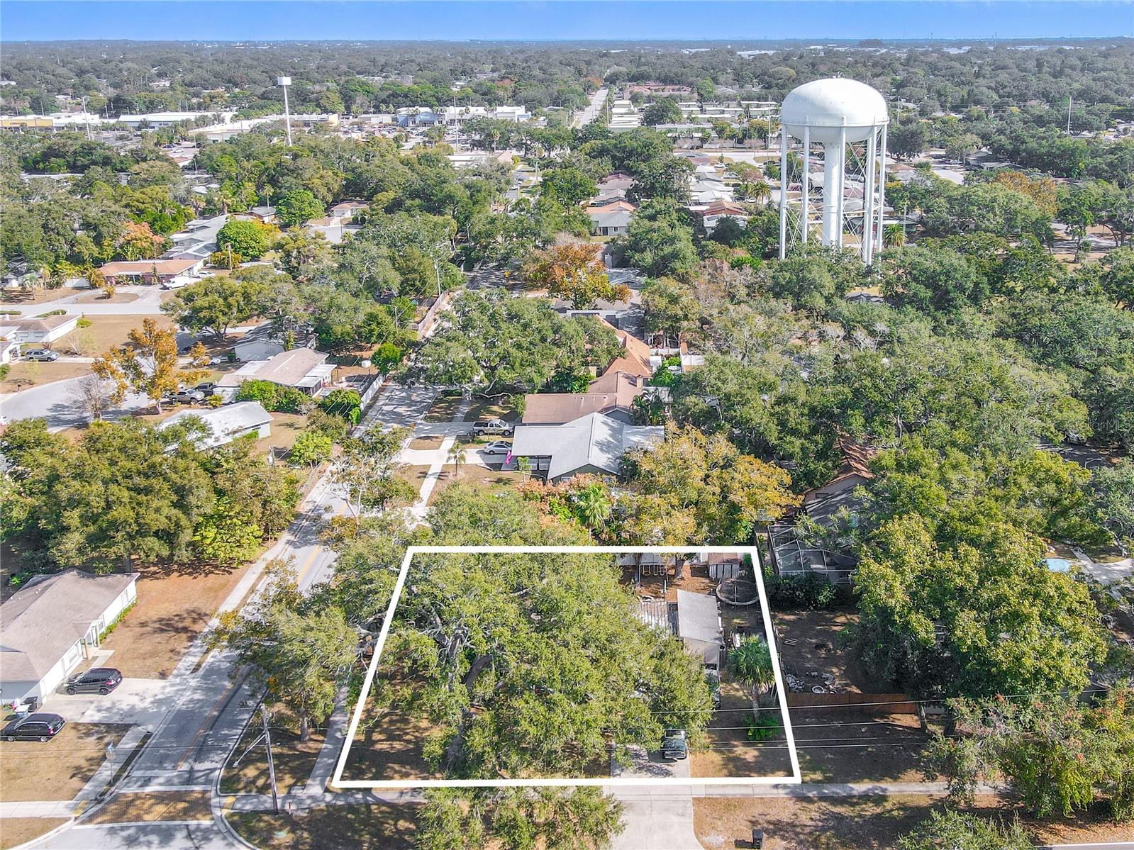 This east-facing aerial view showcases the full expanse of the property, outlined for clarity. Mature trees provide shade and privacy across the lot, while the surrounding neighborhood features well-kept homes and quiet streets. This perspective highlights the generous lot size, the home’s placement, and its convenient proximity to nearby amenities—including the prominent water tower visible in the distance. A standout view for understanding the property’s scale and location.