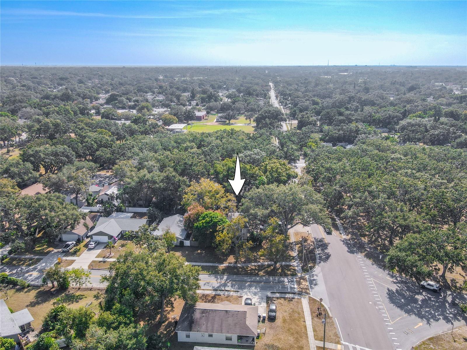 This south-facing aerial view highlights the home’s position within a lush, tree-lined neighborhood. The property is marked with an arrow for easy identification, showcasing its generous lot size and corner location. Surrounded by mature canopy trees and well-kept homes, the area offers a peaceful residential setting with convenient access to nearby parks, schools, and main roadways. A beautiful perspective that captures both privacy and community.