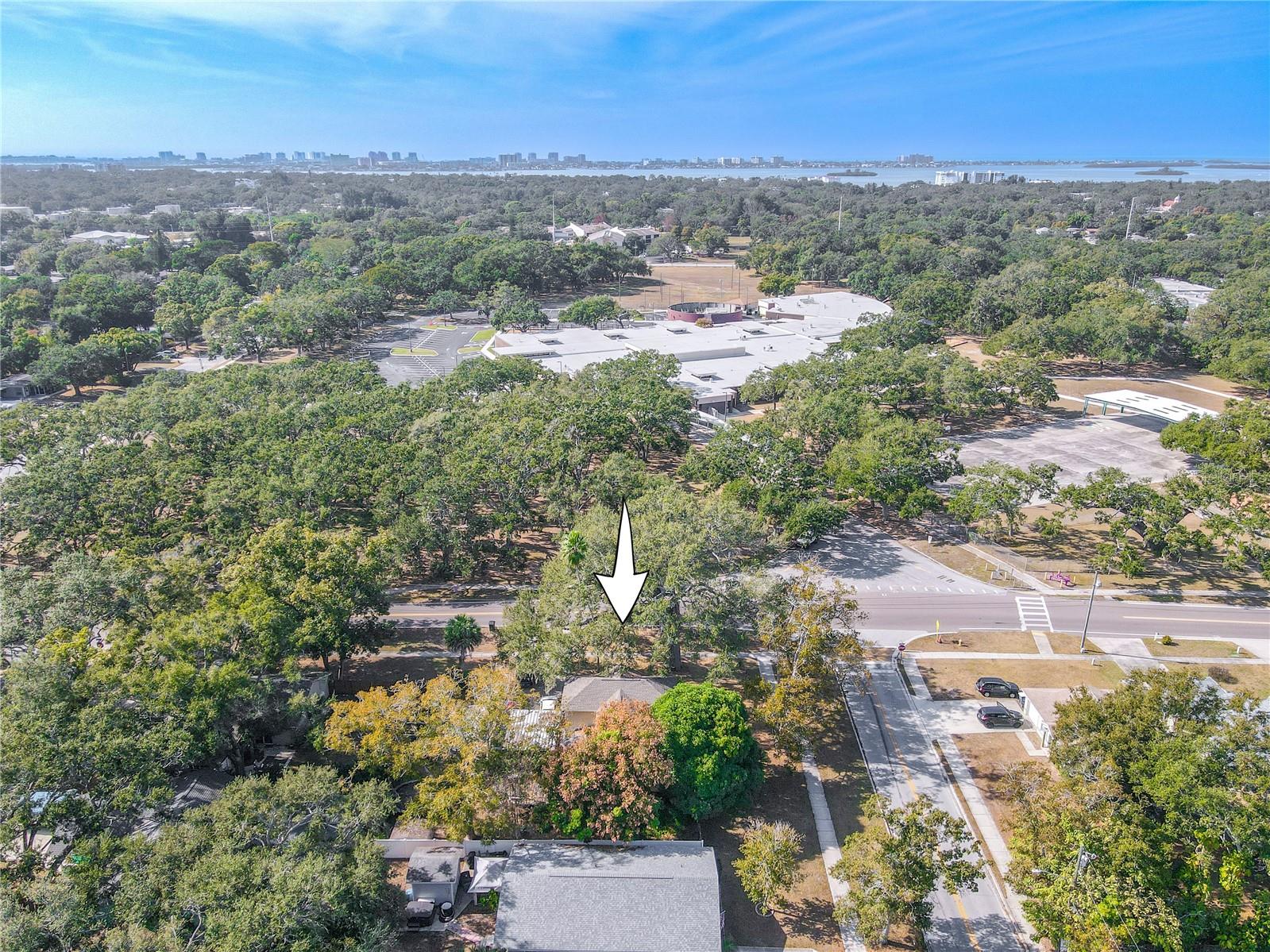 This west-facing aerial view highlights the property’s prime location, marked with an arrow for easy identification. Surrounded by mature trees and tucked within a peaceful residential area, the home sits just moments from nearby schools, parks, and recreational facilities. In the distance, you can see the coastal skyline and waterways, showcasing the area’s close proximity to Florida’s beautiful beaches. This perspective captures both the neighborhood charm and the convenience of the surrounding amenities.