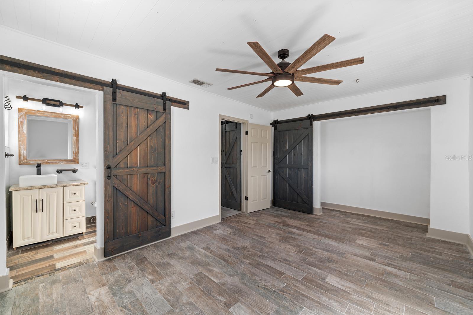 Primary bedroom featuring tile floors, ceiling fan and barn doors