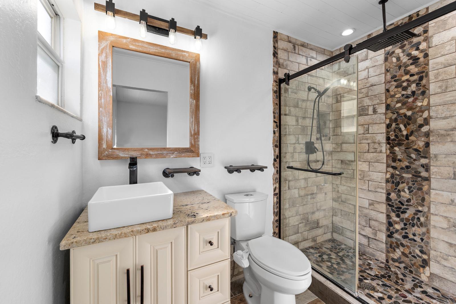 Primary bathroom featuring sleek glass enclosed walk-in shower with river rock accents