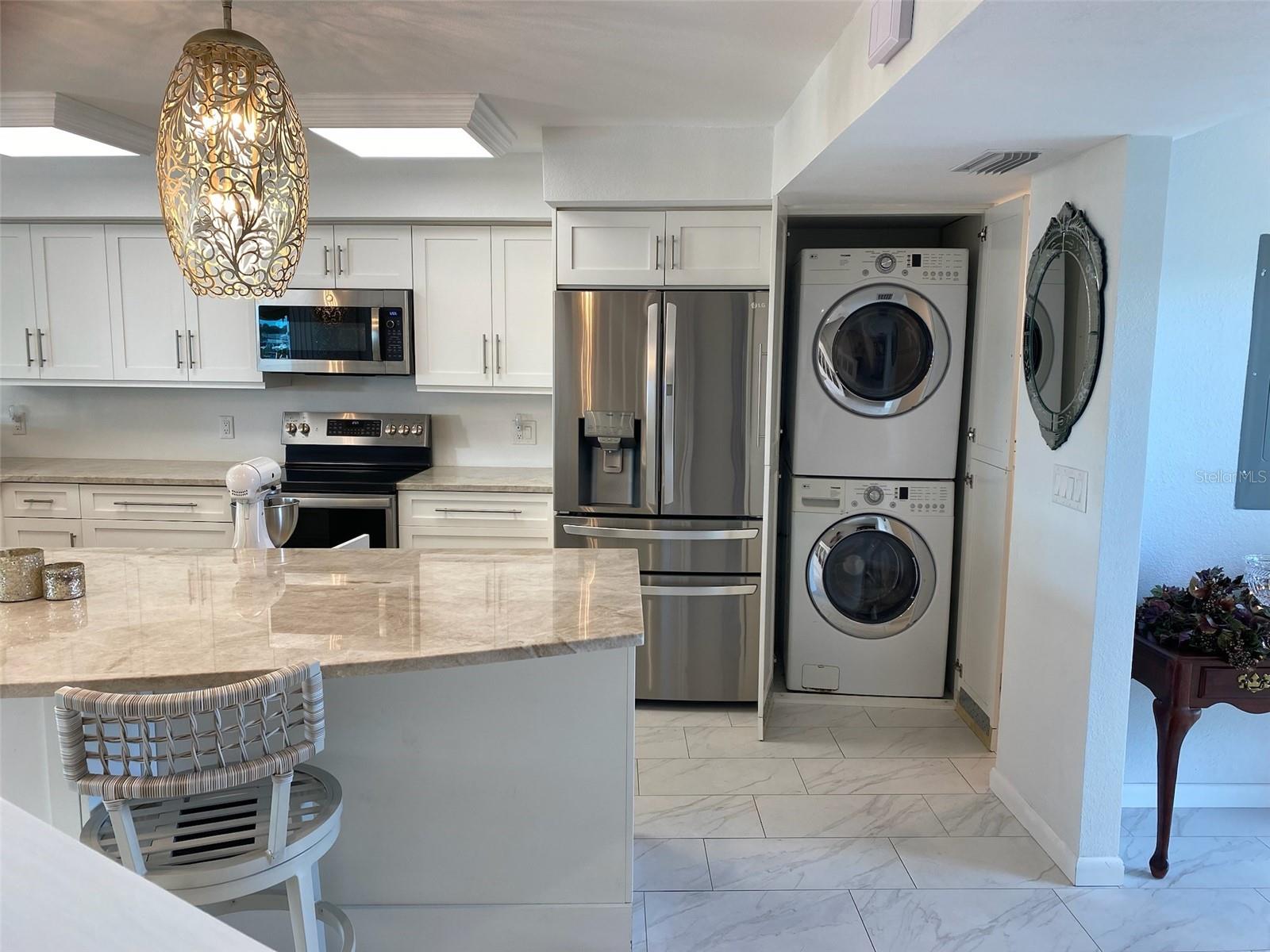 Bright modern kitchen with marble counters, stainless appliances, and a convenient hidden stacked washer-dryer.