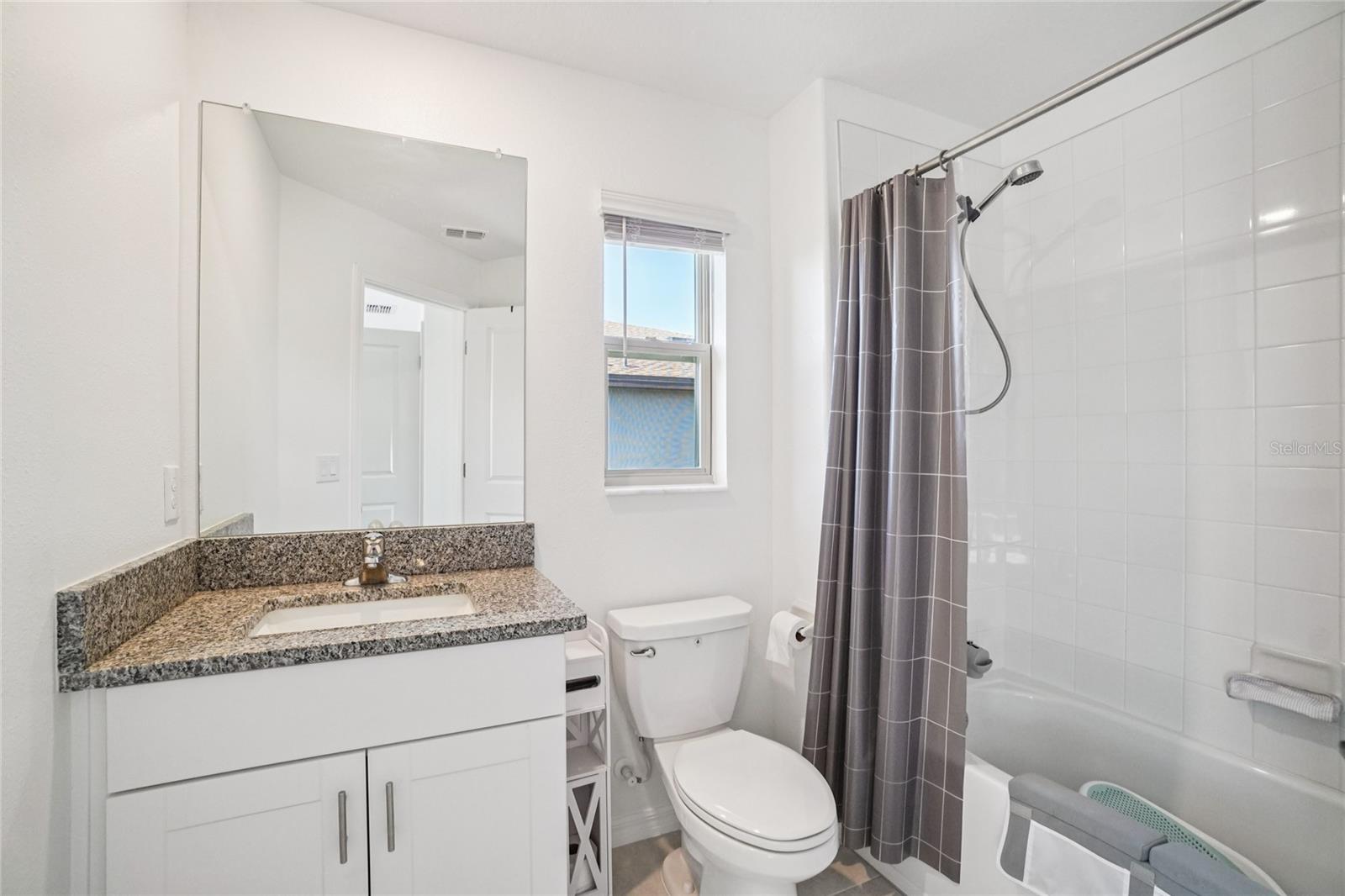 Bed 2 Bathroom – Bright full bath featuring a granite-topped vanity, tiled shower-tub combo, and a window that adds natural light.