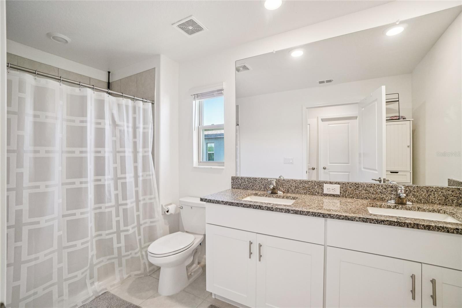 Primary Bathroom – Modern en-suite with a dual-sink granite vanity, ample storage, and a tiled shower-tub combination.