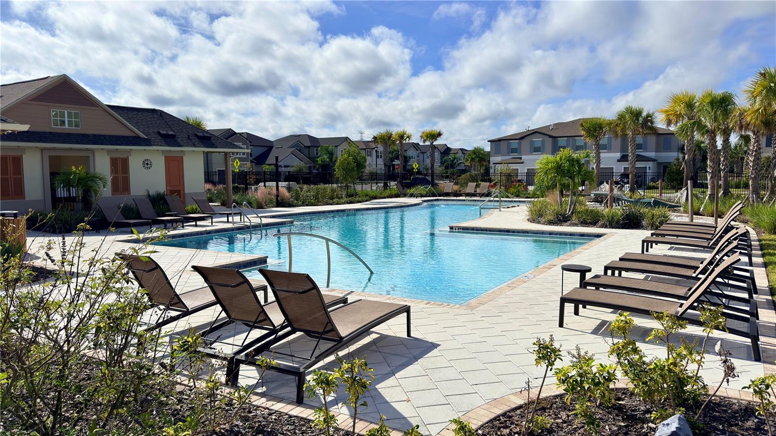 Resort-style community pool surrounded by lush landscaping, plenty of lounge seating, and well-kept common areas, offering a relaxing outdoor space for everyday enjoyment.