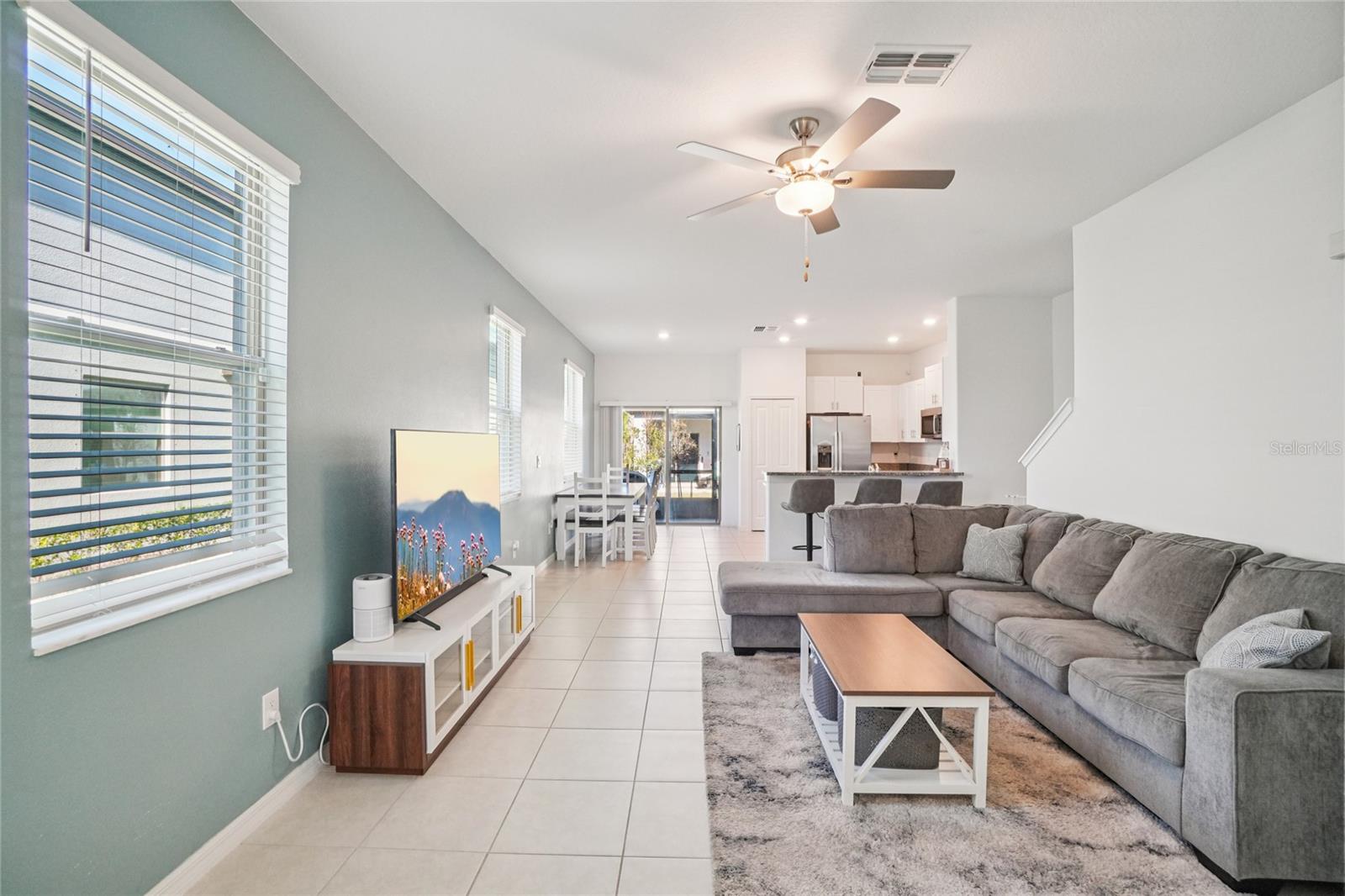 Living Room – Wide View – Spacious living room with tile flooring, multiple windows for natural light, and an open layout flowing into the dining area and kitchen.