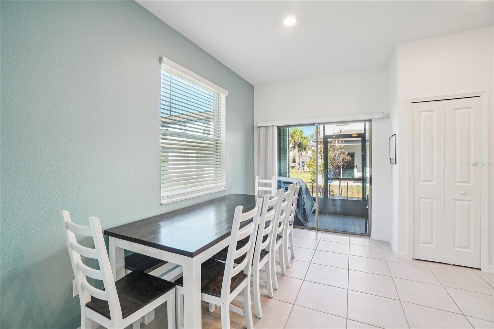 Dining Area – Bright dining space with tile flooring and room for a full-size table, featuring a large window and sliding doors that open to the screened-in patio for easy indoor–outdoor flow.