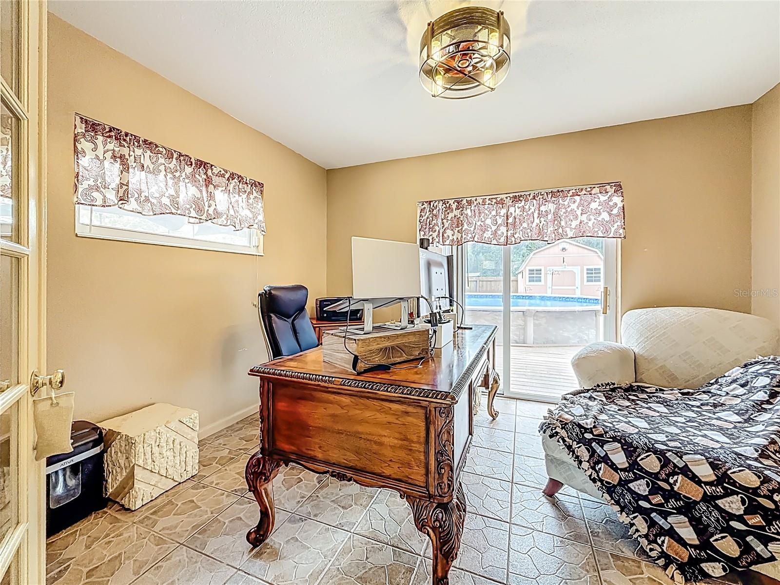 View into the 4th bedroom. Updated sliding glass door leads to the back patio, pool & yard. To the right of the chaise is a wall closet.
