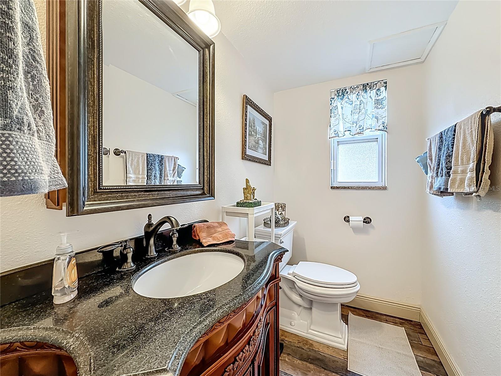 Beautifully appointed half bath in the downstairs hallway, positioned between the dining room and living room. Solid Cherry wood cabinet with granite counter (2019) LVP flooring. The window faces the backyard.
