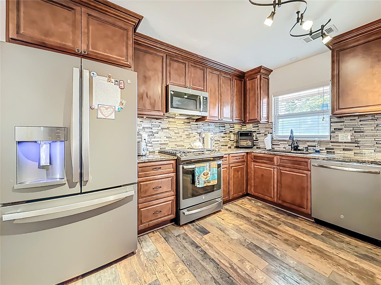 Behind you is the breakfast bar and the view is of the updated kitchen (2019). Solid wood cabinets, soft close doors & drawers, upper cabinets have under cabinet lights, GE Gas range with gridle pan, GE dishwasher, GE Microwave. GE Side-by-side refrigerator (2022),  deep double sink. The window faces the front yard.