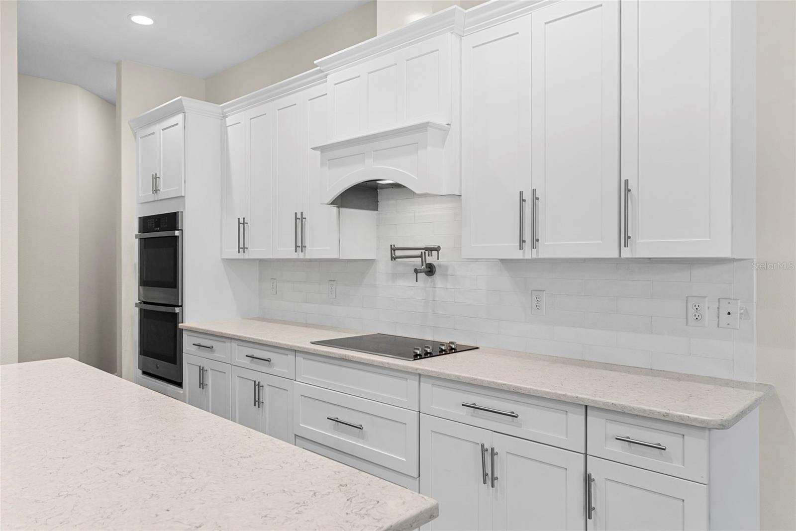 Ample white cabinetry, a built-in double oven, and a sleek cooktop with pot filler create a culinary space that’s both stylish and practical