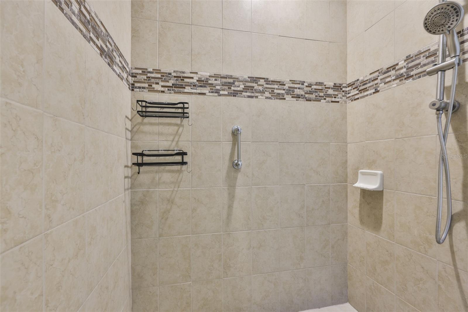 Large, custom, updated tiled bathroom with dual shower heads and handle bars for safety.