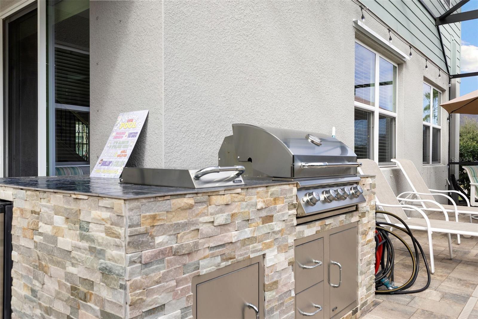 Stone-faced outdoor kitchen equipped with grill, burner, refrigerator and storage