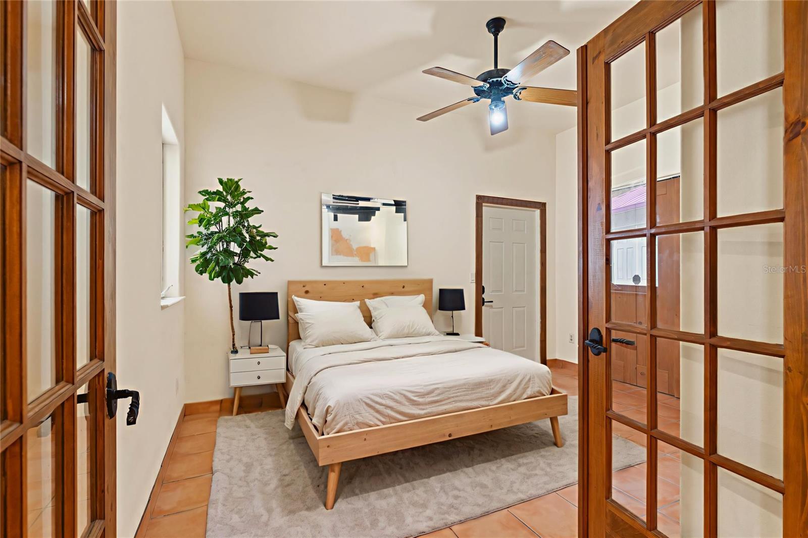 A tranquil bedroom retreat with French doors, light wood furnishings, and a neutral palette, offering peaceful views and privacy.