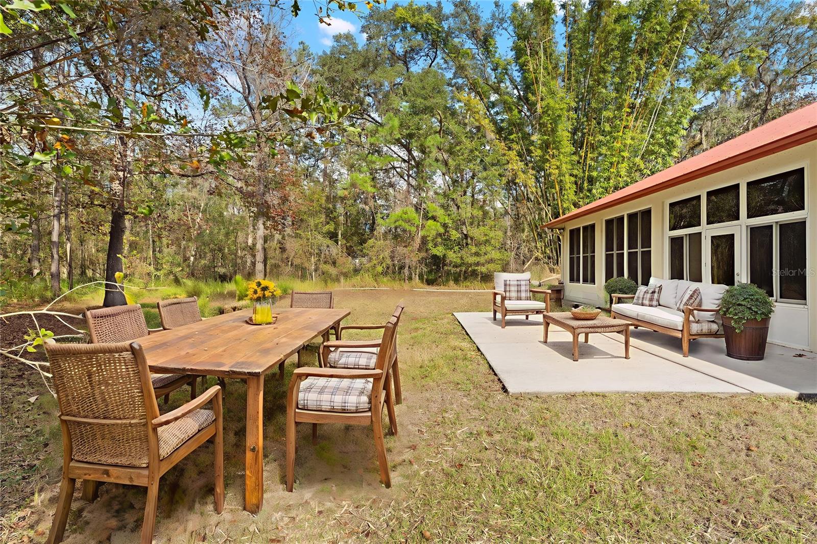 This inviting backyard patio features both lounge seating and a rustic wood dining table, ideal for entertaining or enjoying meals surrounded by lush woodland views.