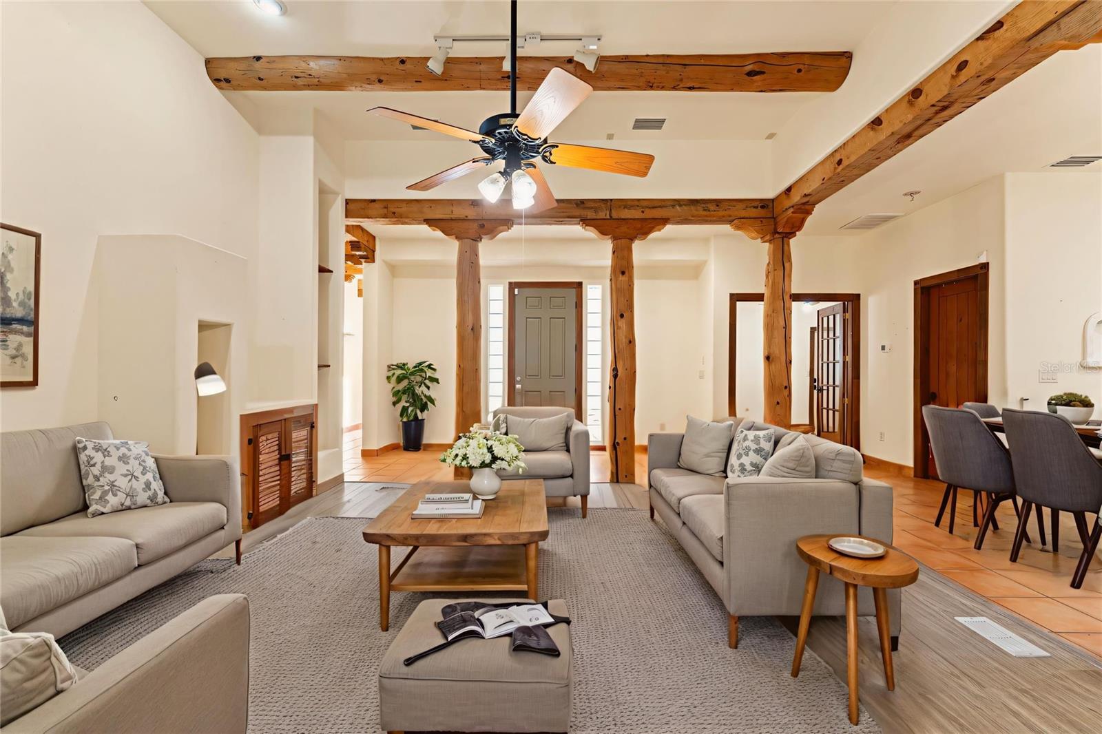 A warm, open living space highlighted by exposed log beams, wood-framed ceilings, and neutral-toned furnishings. The seamless layout flows into the kitchen, creating a cozy and functional gathering area.