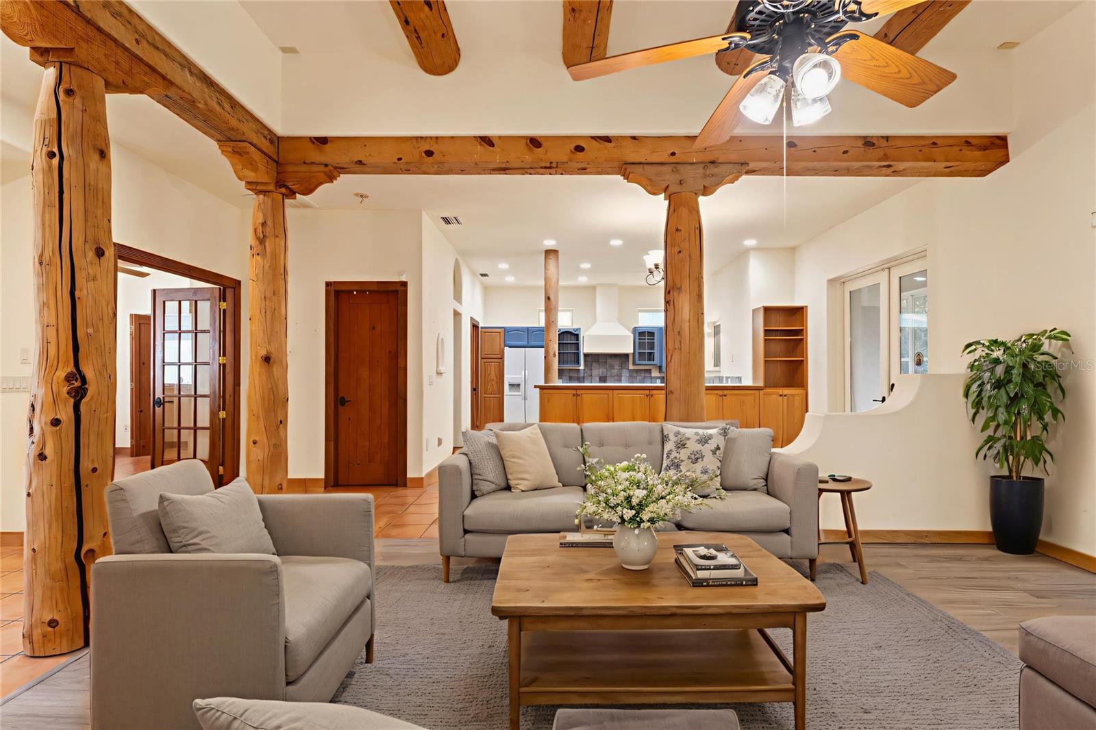 Another angle of the spacious living room showcases natural wood details, tile and plank flooring, and ample natural light from adjacent entryways and windows.