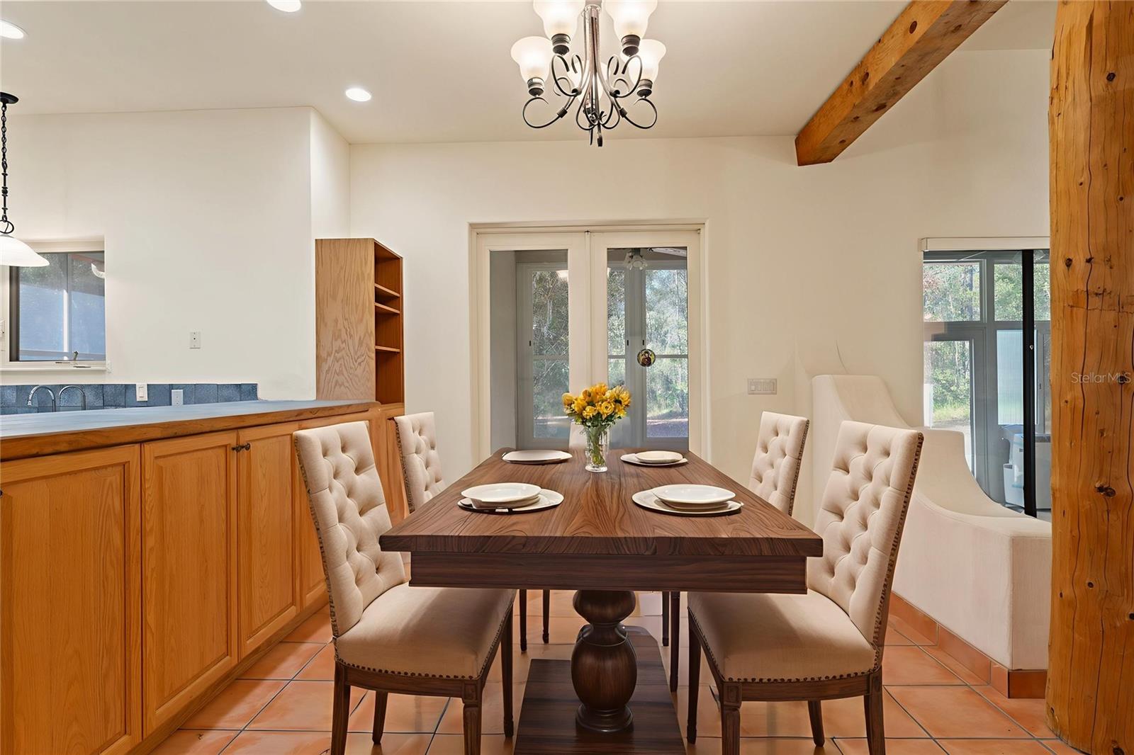 A bright and welcoming dining space with elegant upholstered chairs, wood-beam accents, and access to the outdoors via double glass doors.