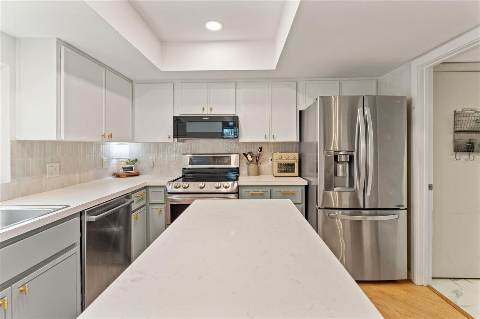 Bright, updated kitchen featuring white upper cabinetry, contrasting lower cabinets, quartz countertops, stainless steel appliances, and recessed lighting.