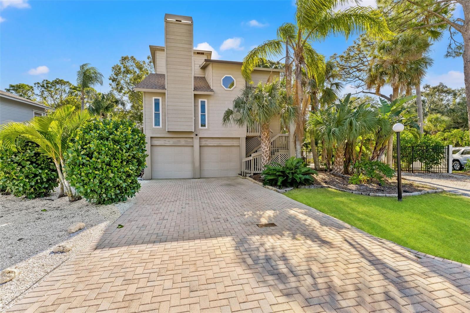 Brick paver drive leads to the garage, surrounded by low-maintenance shell landscaping and manicured greenery.