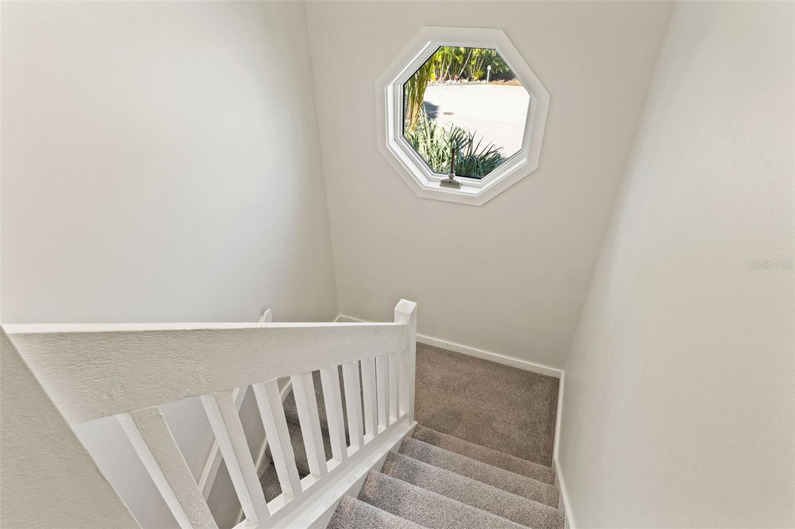 Carpeted staircase with white railing and an octagonal window that fills the stairwell with natural light.