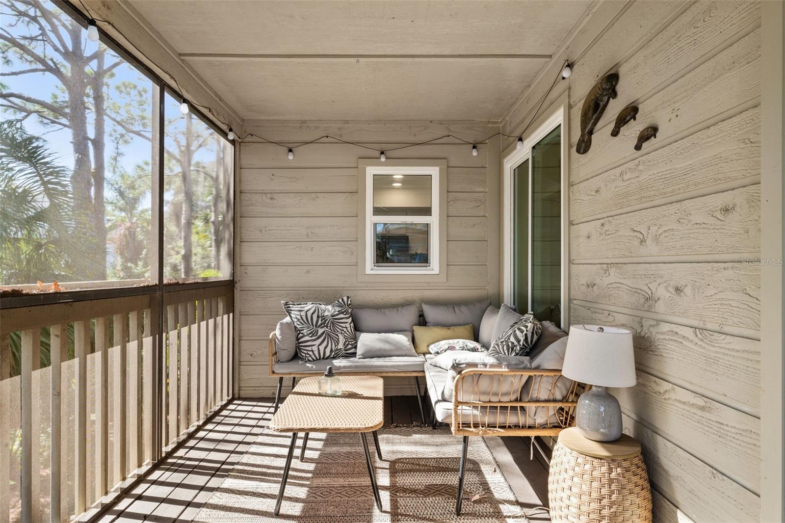Inviting screened porch with wood decking, string lighting, ceiling fan, and seating area—ideal for relaxing or entertaining.