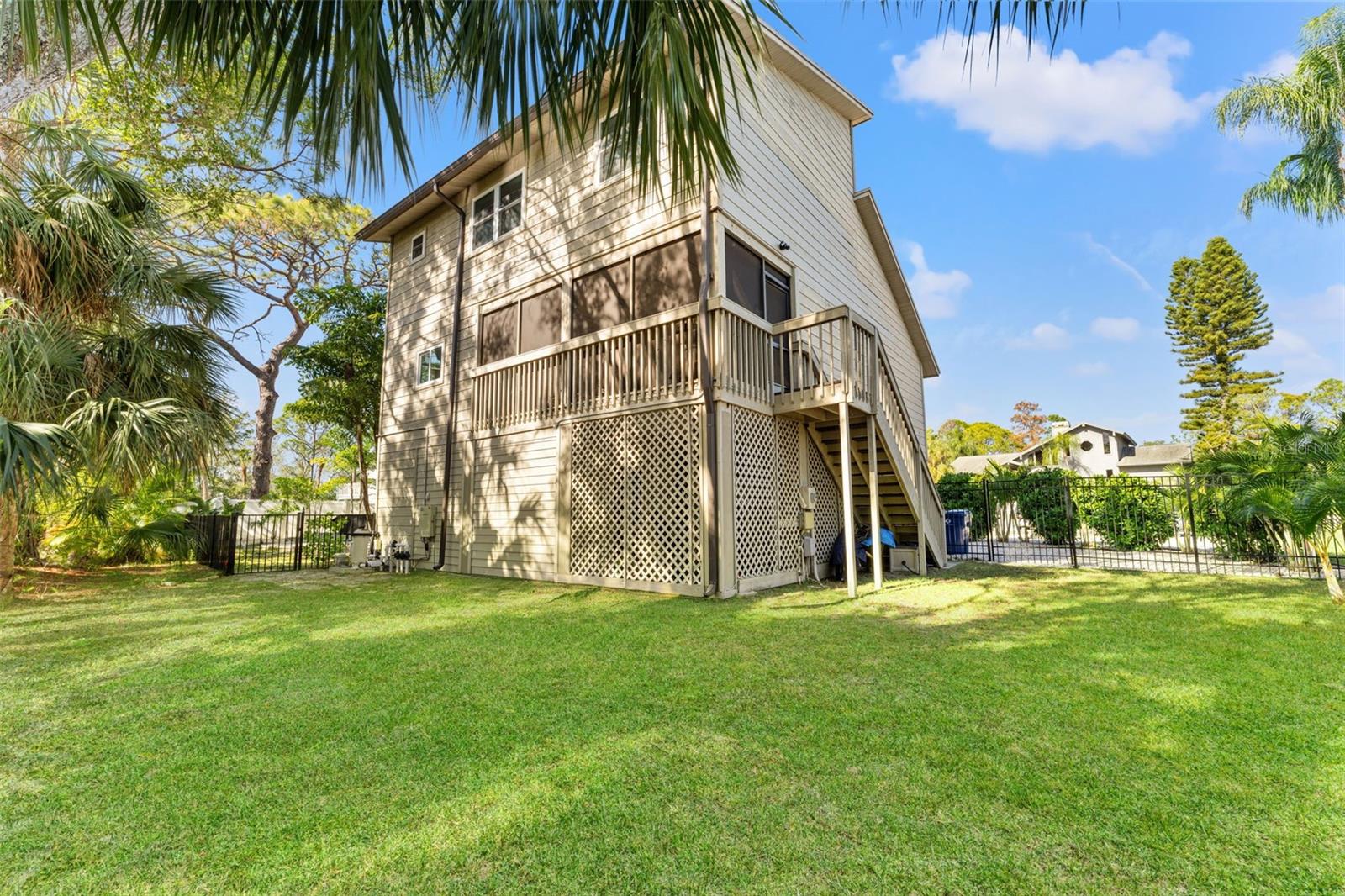 Rear exterior view highlighting the elevated home design, exterior staircase, lattice detail, and screened porch above.
