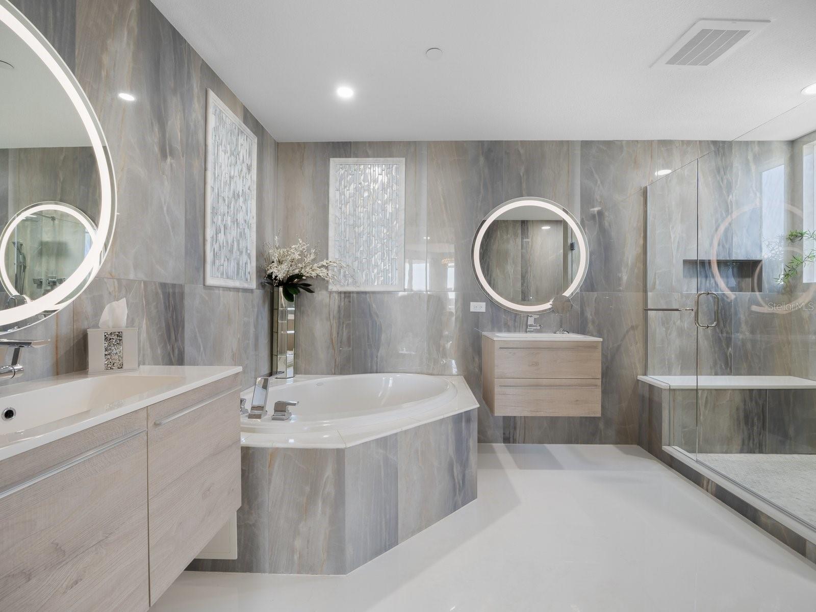 Gorgeous primary bathroom with double vanity, illuminated lighting, porcelain tile, tub and walk-in shower