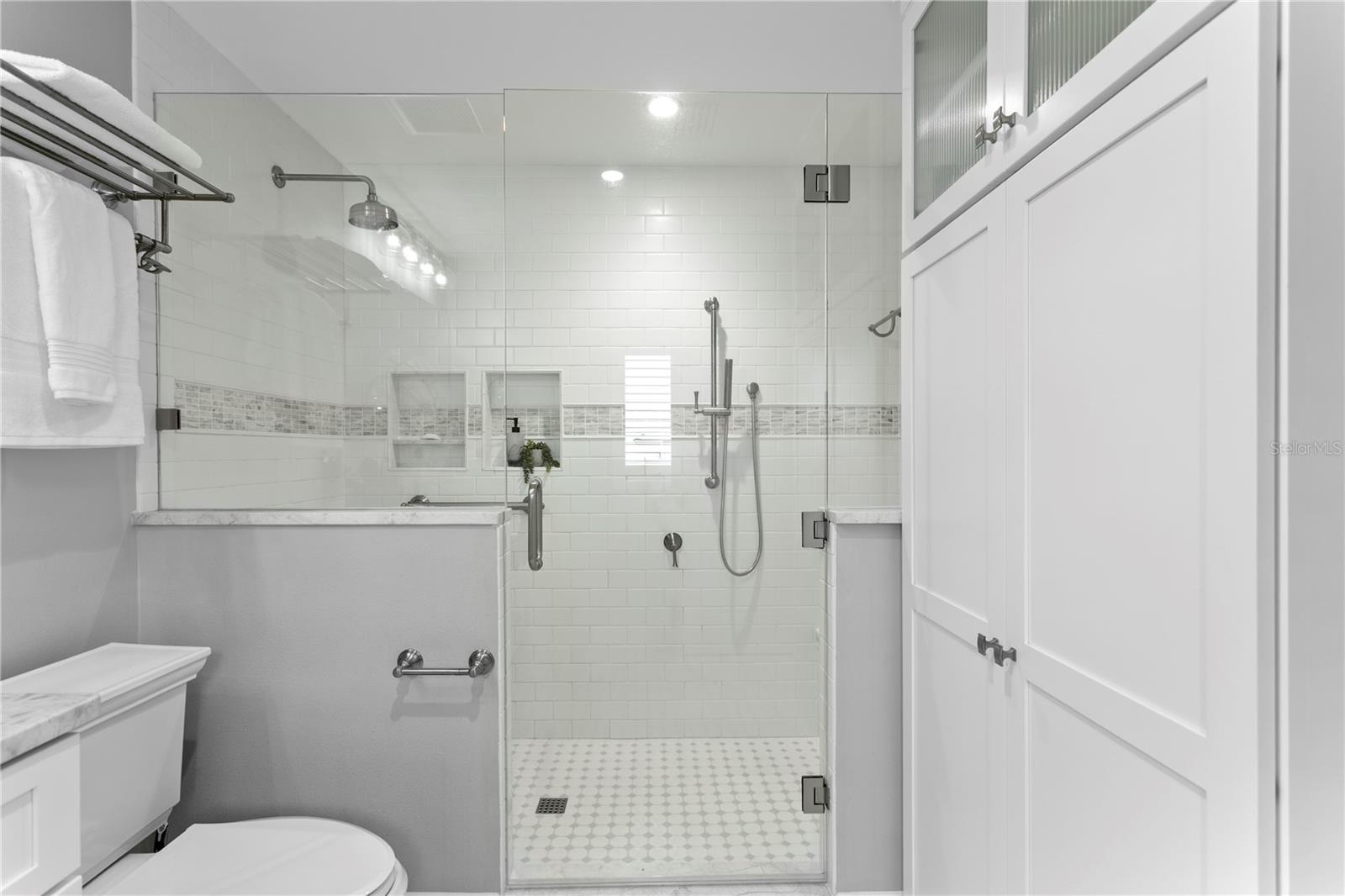 Primary bath boasts large walk-around shower with bench and custom floor-to-ceiling cabinetry