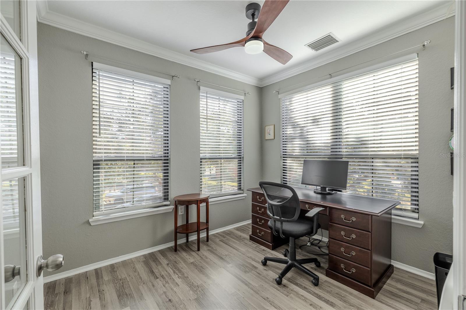 The primary bedroom offers a calm retreat with wood-look flooring, a modern ceiling light, wall-mounted TV, and sliding glass doors that open directly to the private balcony, filling the room with natural light.