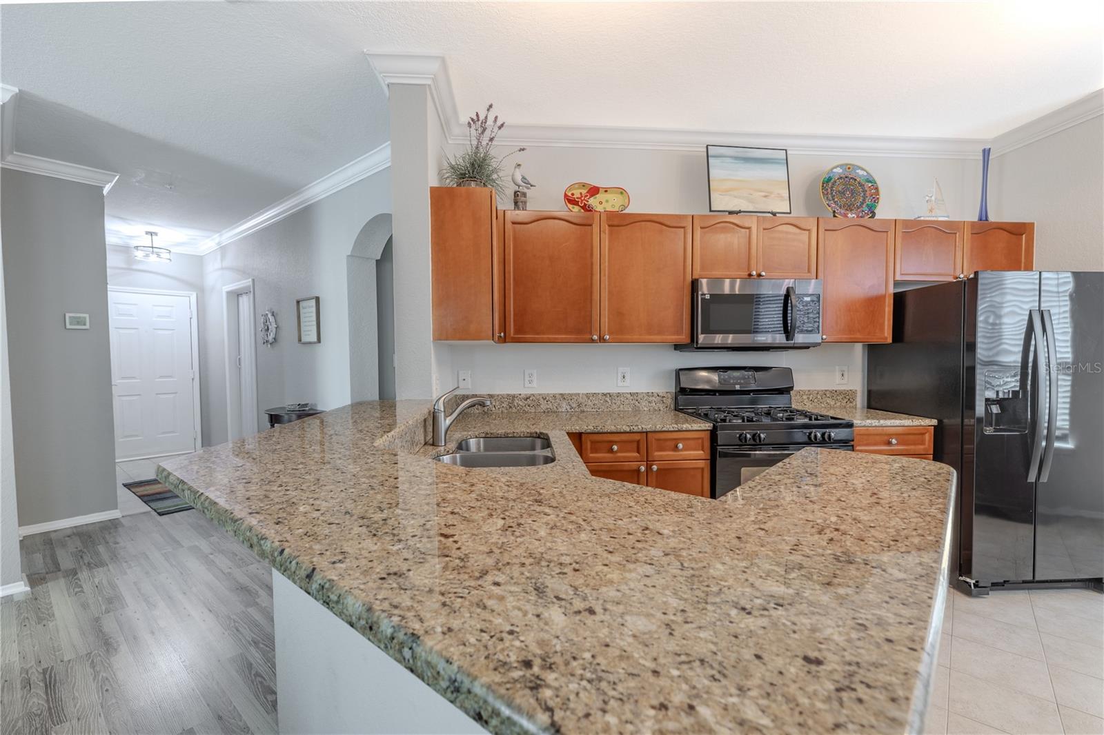 This angle highlights the kitchen’s efficient layout with granite countertops, warm wood cabinetry, stainless appliances, and a spacious breakfast bar that opens directly to the living area, enhancing both functionality and flow.