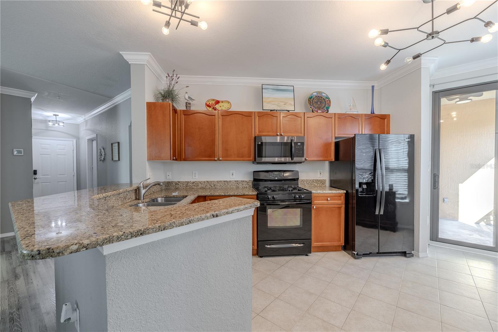 This kitchen view highlights the spacious walk-in pantry with built-in shelving, along with granite countertops, stainless appliances, warm wood cabinetry, and an open sightline to the living area for easy everyday living and entertaining.