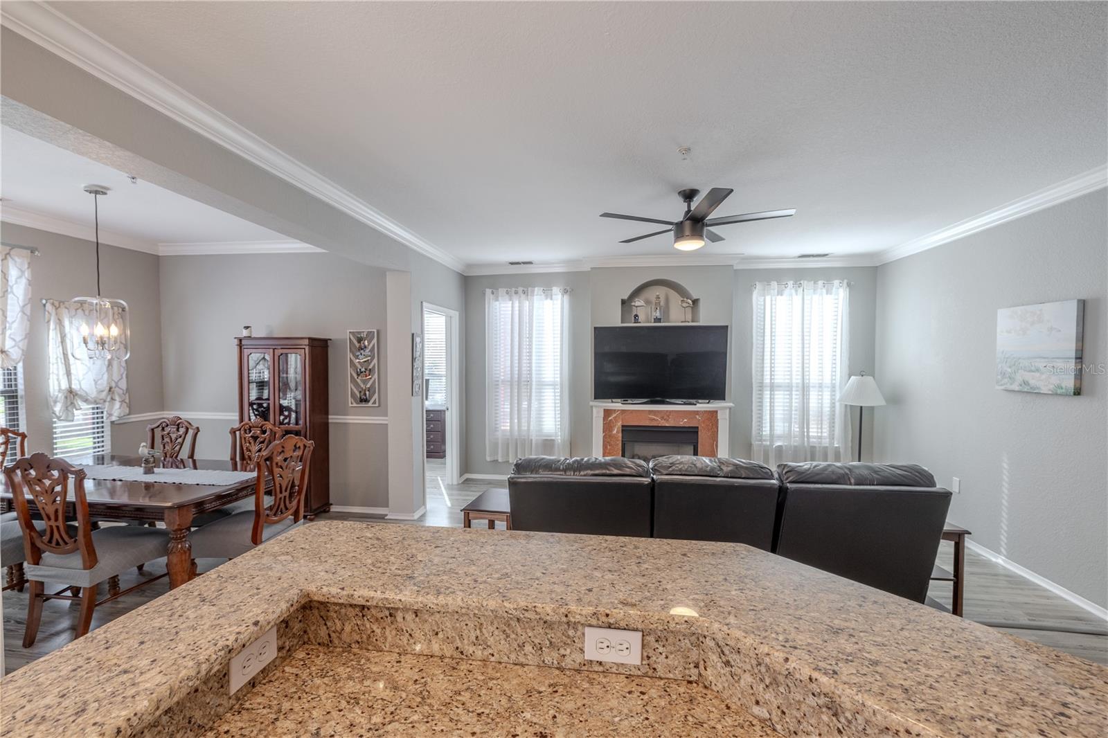 This angle showcases the bright living room centered around a cozy fireplace, framed by tall windows, crown molding, and modern lighting that enhance the room’s open, airy feel.