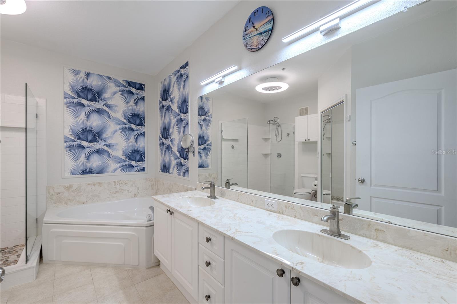 This view highlights the spa-inspired primary bathroom with a glass-enclosed walk-in shower featuring pebble-style flooring, a deep soaking tub with elegant tile surround, and bright, contemporary finishes throughout.