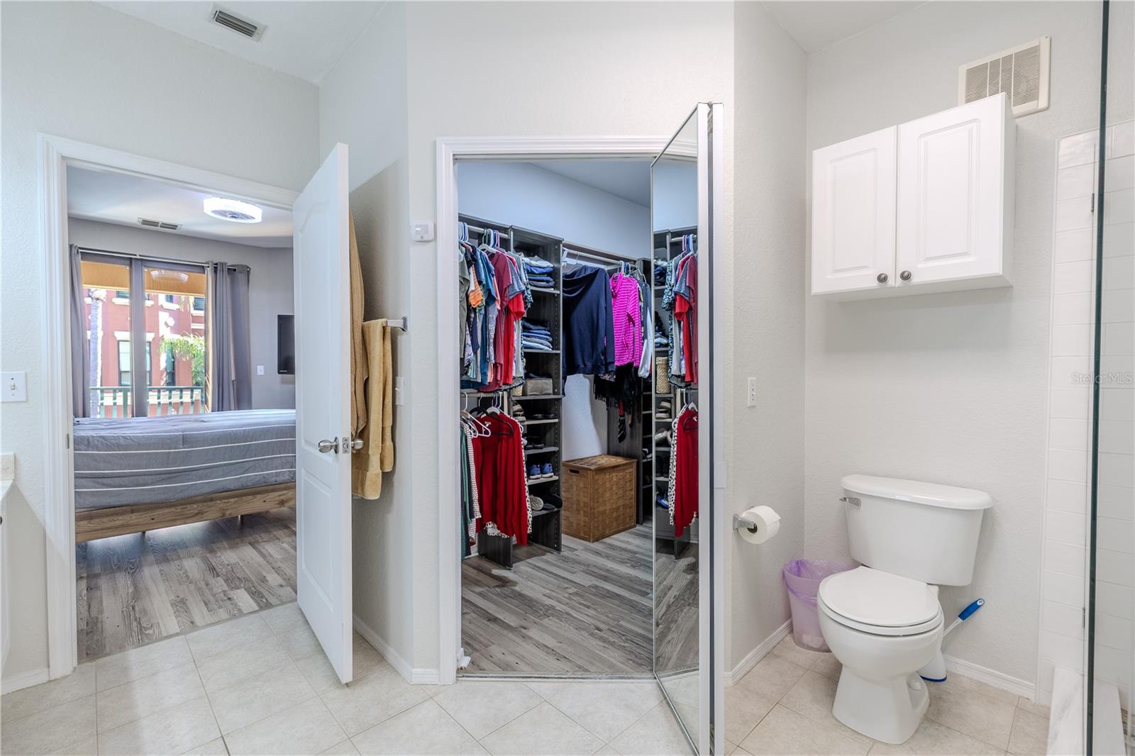 This bright second bedroom features multiple windows for natural light, neutral finishes, wood-look laminate flooring, and ample space to function comfortably as a guest room, home office, or flex space.