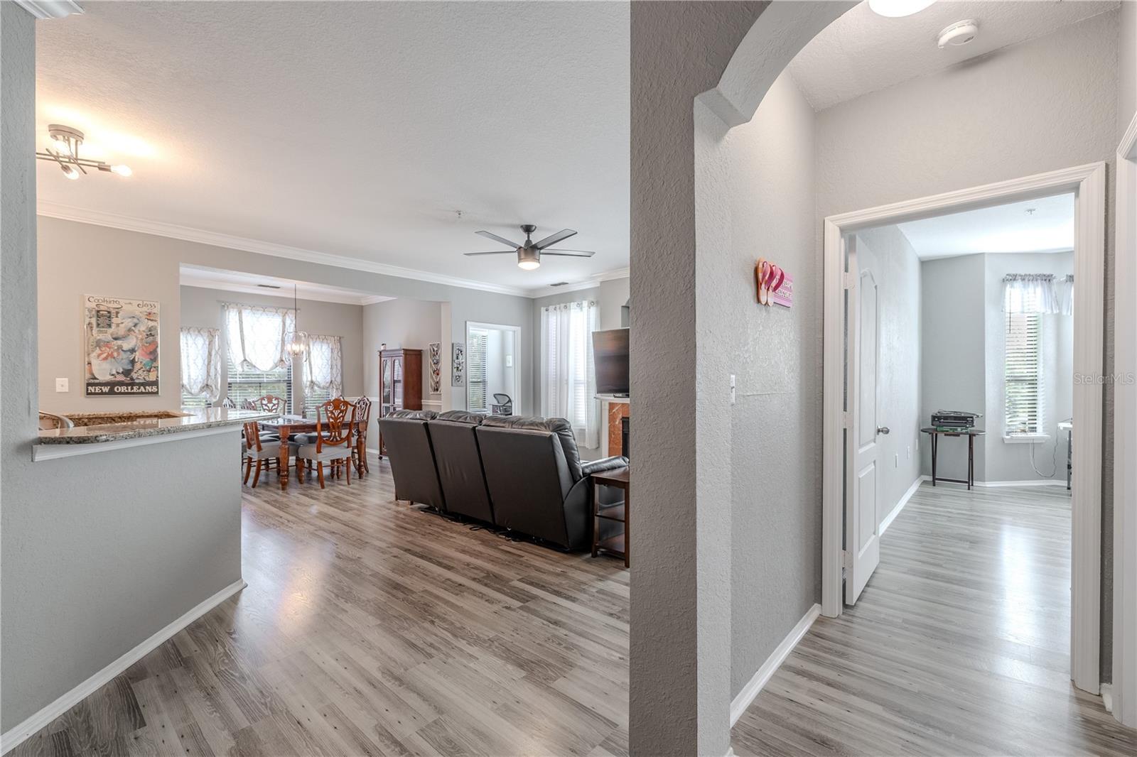 This alternate view of the second bedroom highlights the spacious layout, ceiling fan, wood-look laminate flooring, and a generous double-door closet, with easy access to the main living areas just outside the doorway.