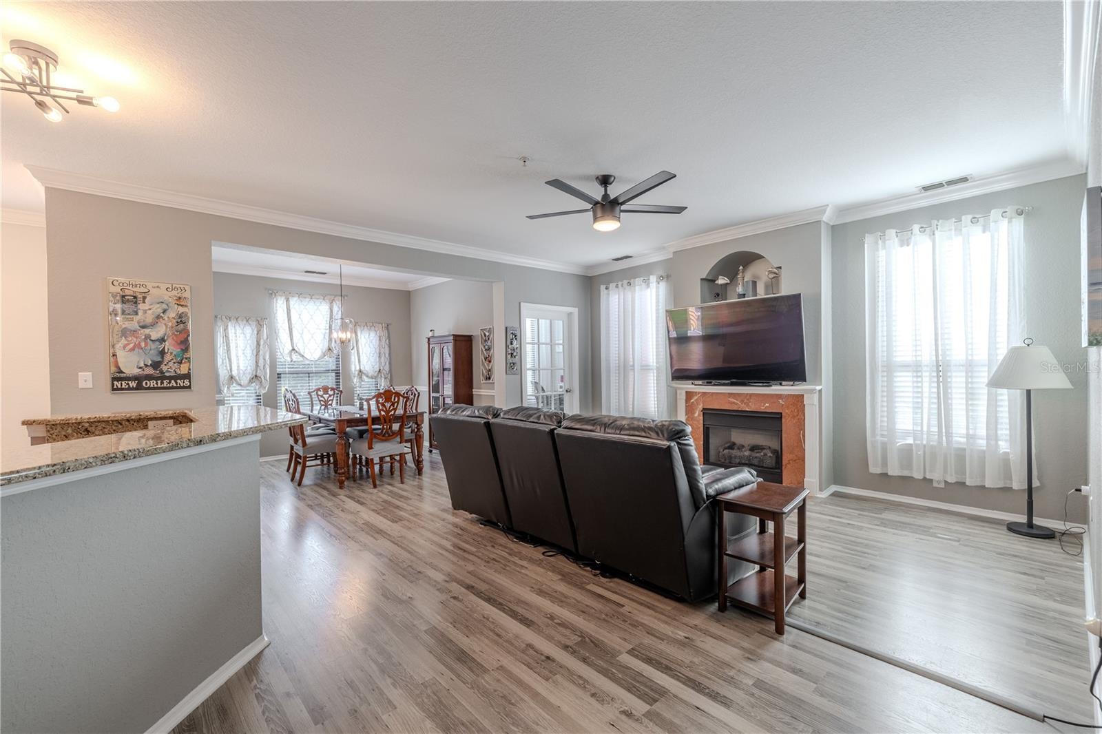 An expansive open-concept layout connects the living room, dining area, and kitchen, featuring crown molding, wide-plank flooring, modern lighting, and seamless flow ideal for everyday living and entertaining.