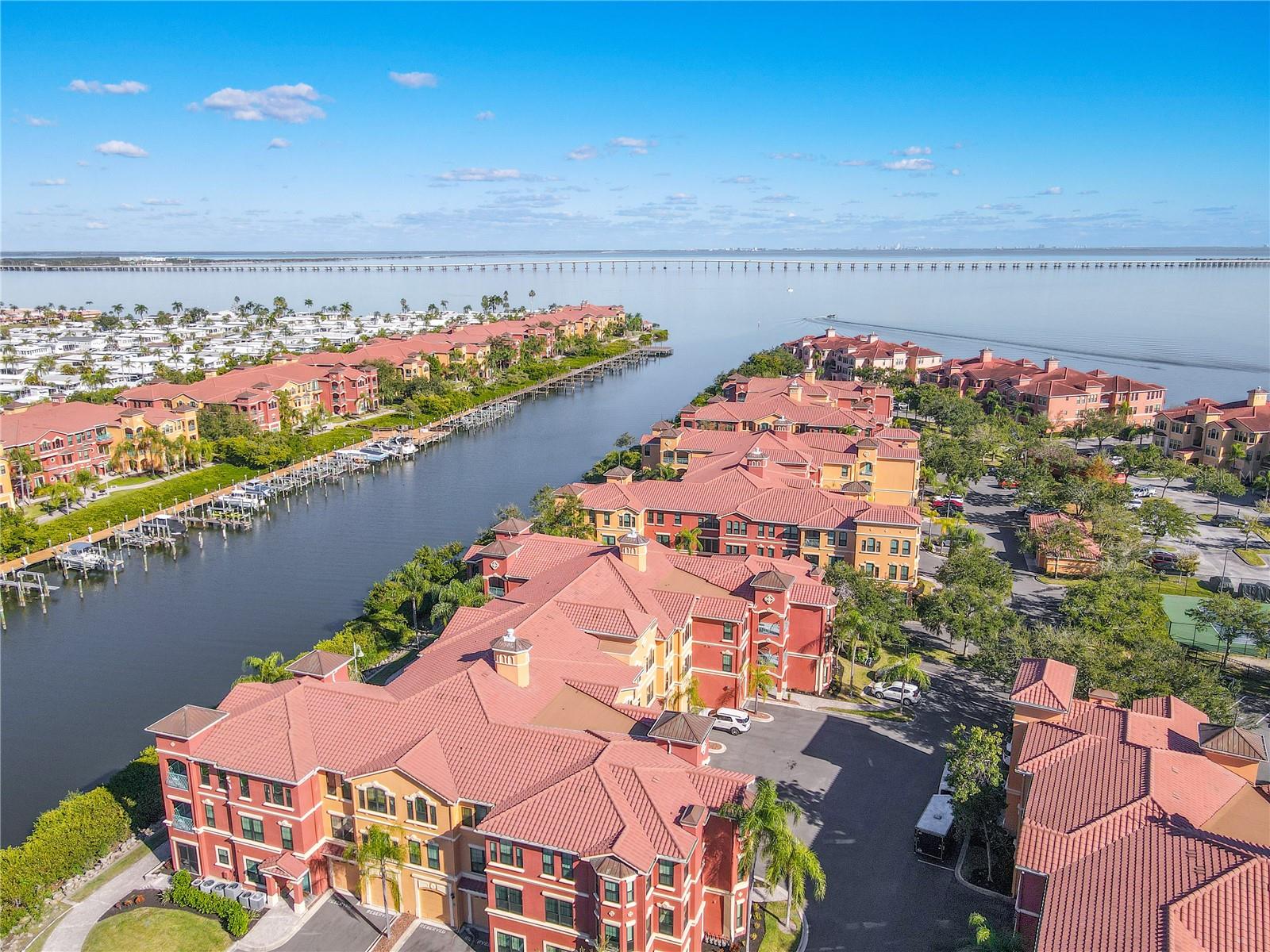 An elegant aerial captures the beautifully designed Mediterranean-style building, highlighting the second-floor corner residence within a lush, palm-lined courtyard setting.