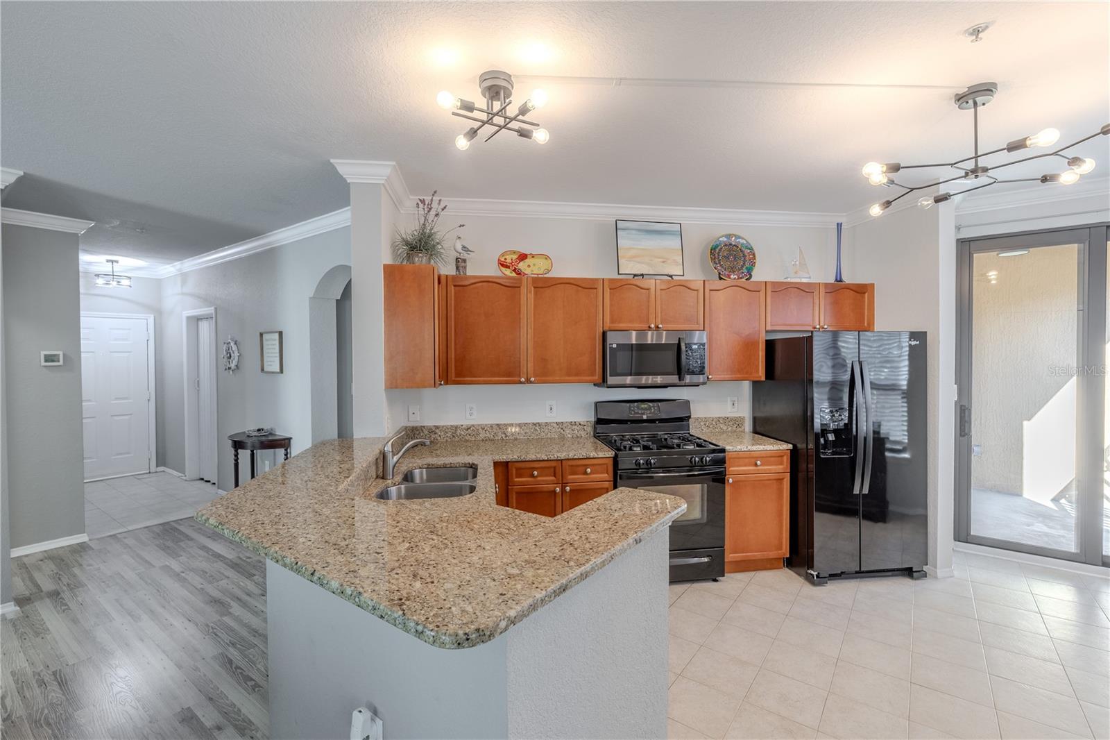 A well-designed kitchen combines expansive granite counters, a generous breakfast bar, warm wood cabinetry, stainless appliances, and modern lighting, all opening seamlessly to the private balcony for effortless indoor–outdoor living.