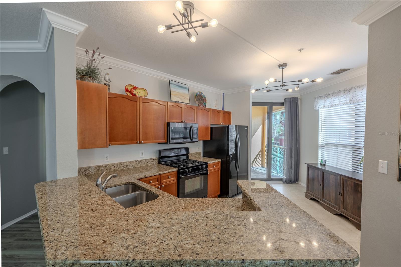 An expansive granite breakfast bar anchors the kitchen, complemented by warm wood cabinetry, stainless appliances, and an open sightline to the foyer and living areas for effortless entertaining.