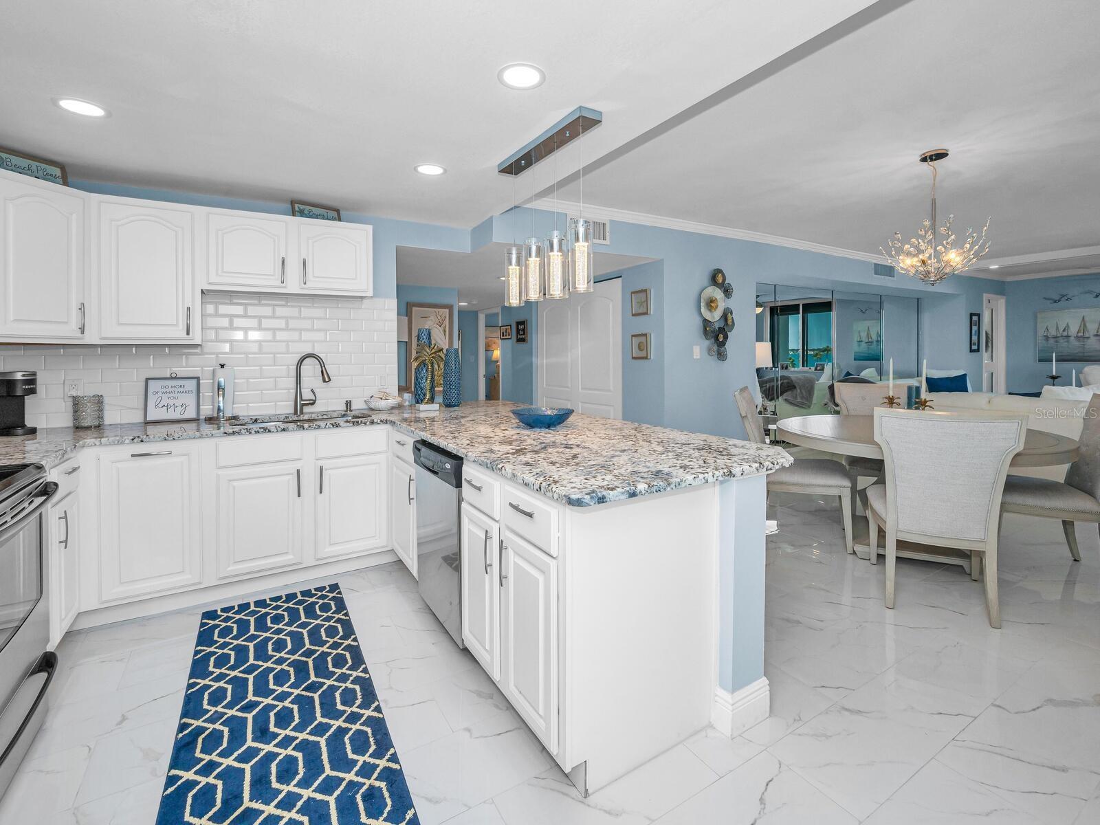 Custom Designed Open Cucina with granite surfaces, custom wood cabinetry, backsplash, recessed & pendant lighting equipped with stainless appliances.