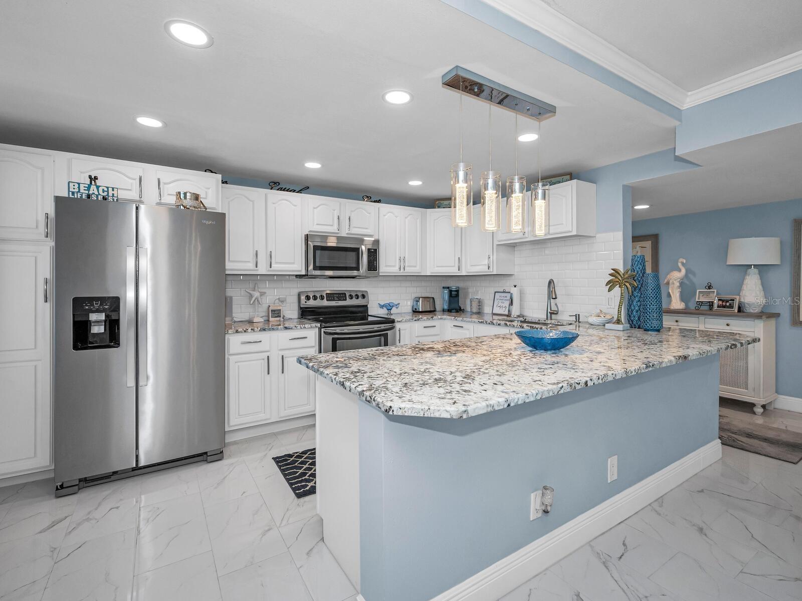 Custom Designed Open Cucina with granite surfaces, custom wood cabinetry, backsplash, recessed & pendant lighting equipped with stainless appliances.