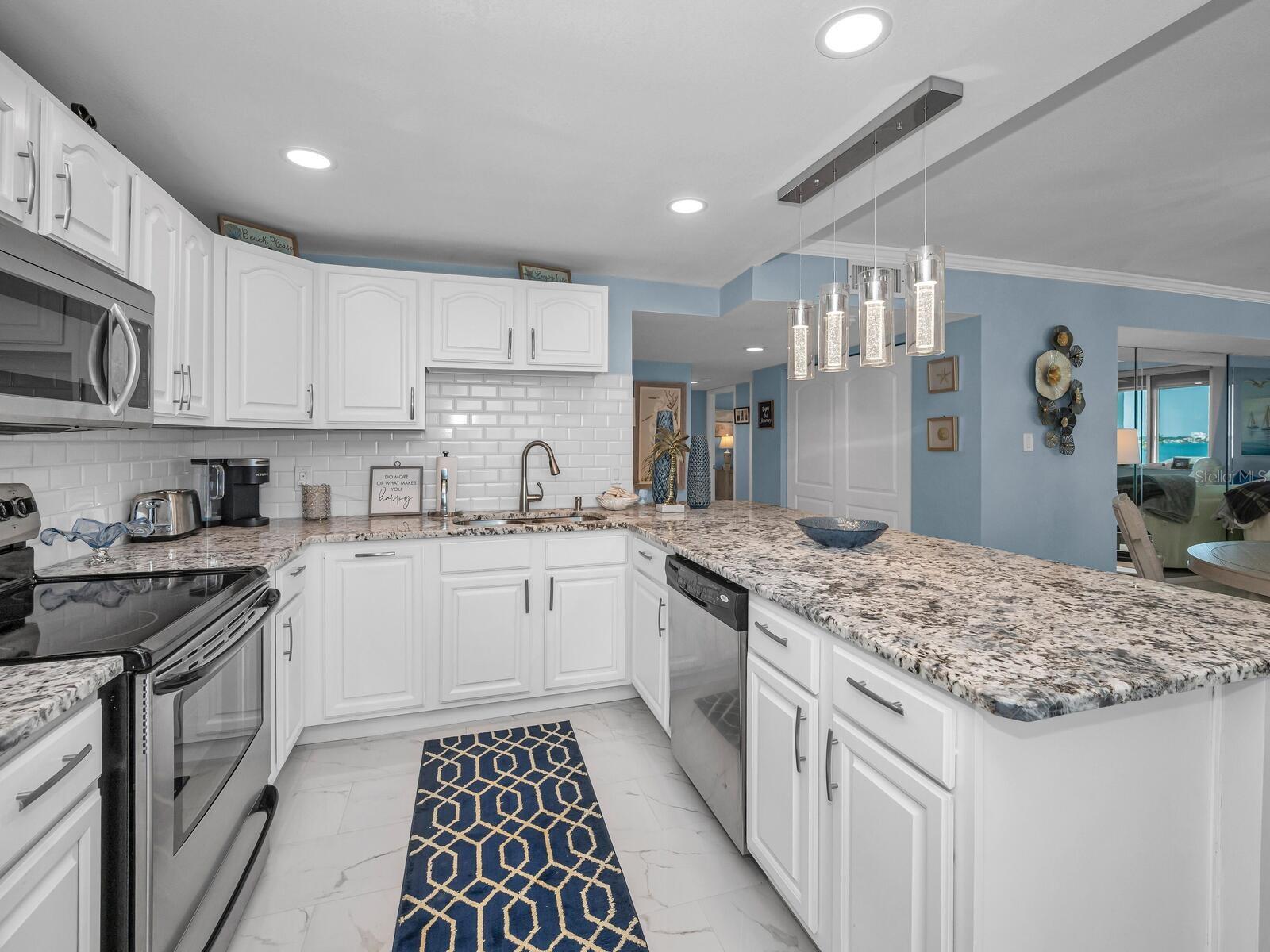 Custom Designed Open Cucina with granite surfaces, custom wood cabinetry, backsplash, recessed & pendant lighting equipped with stainless appliances.